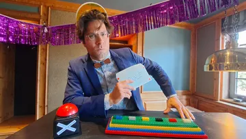 Man in suit holding card, playing table with keys in front of him.