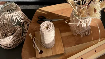Ein Garnrolle liegt neben Makramee-Projekten auf einem Tisch.