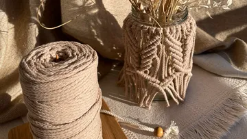 Garnrolle neben dekorativem Glas mit Trockenblumen steht.