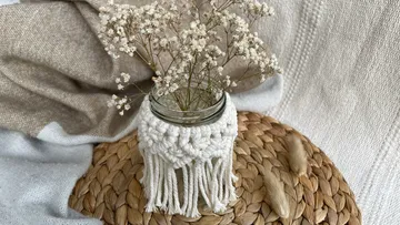Glasvase mit zarten Blumen auf einem geflochtenen Untersetzer.