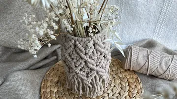 Vase mit Trockenblumen auf einem geflochtenen Untersetzer.