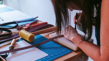 Woman is working on a piece of leather on a table.
