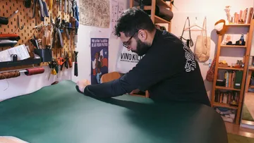Craftsman works green leather in a workshop environment.