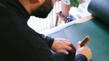 Man is drawing on green leather in a work room.