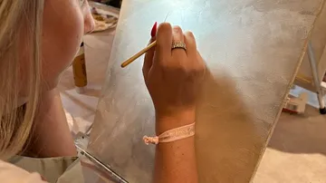 A woman paints on a blank canvas with a brush.