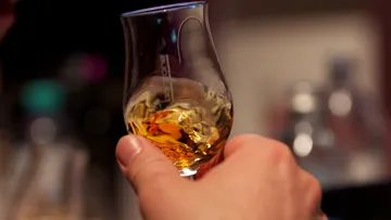 Ein Glas mit goldenem Getränk wird gehalten.