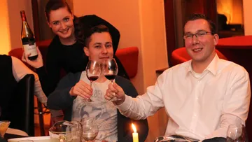 Drei Personen heben Gläser, feiern in einem Restaurant.