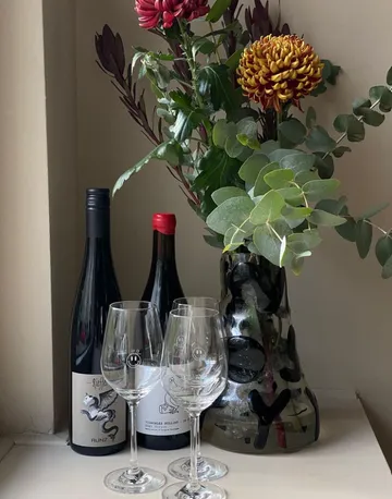 Wine glasses stand next to bottles in a decorative vase.