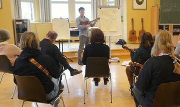 Musikunterricht mit einem Lehrer und mehreren Sitzenden.