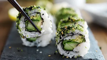 Sushirolle auf einem Steinbrett wird mit Stäbchen gehalten.