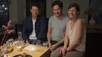 Three people sit together at a table in an interior.