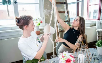 Two women work together to hang a flower.