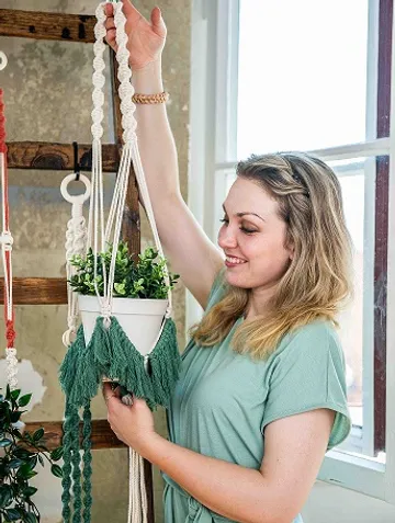 Woman holding up a macrame style flower pot.