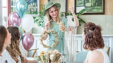 Frau präsentiert kreatives Kunstwerk vor feierlicher Tischgesellschaft.