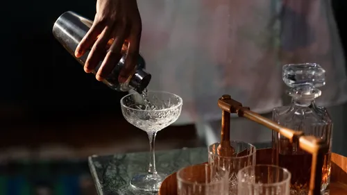 Ein Hand schüttelt Cocktails in ein Glas auf einem Tisch.