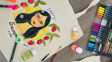 Tasche mit gemalter Figur und Sommerbotschaft, umgeben von Farben.
