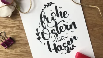 Handschriftliche Osterkarte liegt auf Holzoberfläche mit Büroklammer.