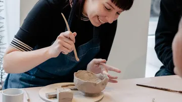 Woman sculpting a clay bowl in a bright room.