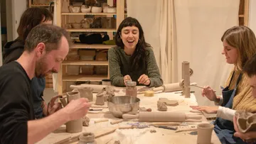 Six people are sculpting ceramics at a table.