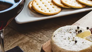 Rotwein neben Käse und Crackern auf einem Holztisch.
