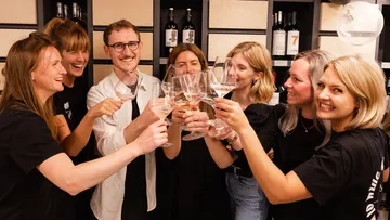 Gruppe von Personen hebt Gläser zum Anstoßen in einem Raum.