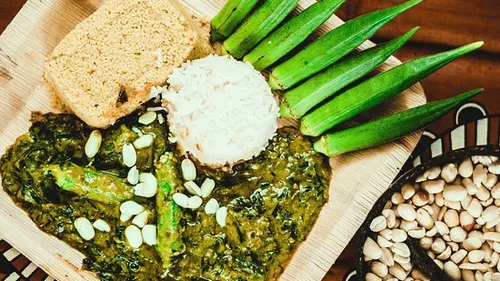 Grünes Gericht mit Reis, Okra und Brot auf Holzplatte.