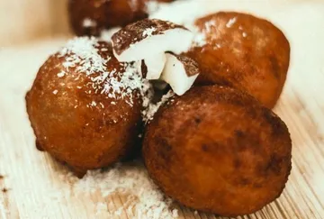 Frittierte Kugeln mit Kokosraspeln auf Holzunterlage.