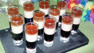 Colourful shot glasses are placed on a black serving board.