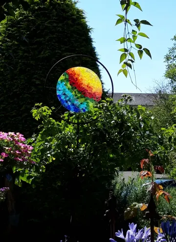 Bunte Windspiel drehend im Garten zwischen Pflanzen und Blumen.