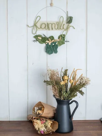 Wall decoration with “family” hangs over a flower vase.