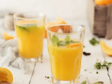 Glasses of yellow drink are on a table.