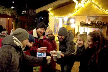 Group of people toasting with hot drinks at festive outdoor market.