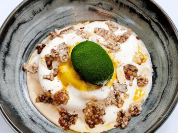 Green dessert plate with yoghurt, yellow, and crispy pieces.