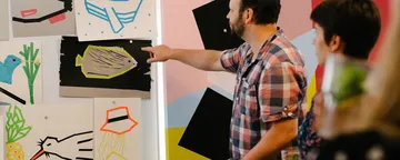 Man points to colorful drawings on the wall.