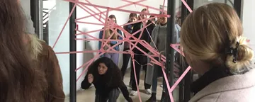 A woman crawls through a pink ribbon net in a room.