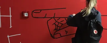 A person draws a hand on a wall with adhesive tape.