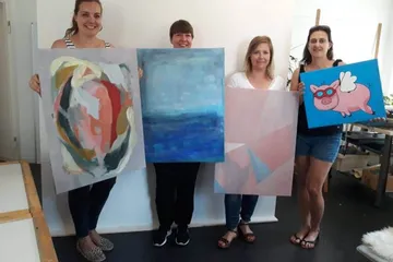 Vier Frauen halten bunte Gemälde in einem Atelier.