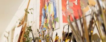 Pinsel stehen in einem Atelier mit bunten Gemälden.