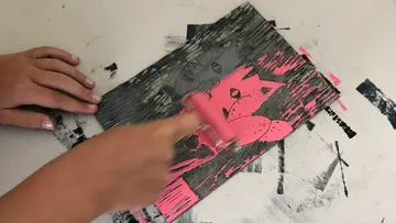 Ein Hände rollen Farbe auf ein Holzschnitt-Muster.