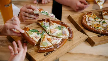 Pizza wird geteilt, umgeben von Händen und Holzplatten.