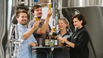 Vier Personen heben Biergläser in einer Brauerei.