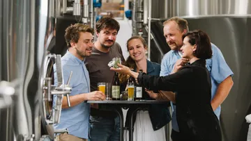 Five people are standing at a table and discussing drinks.
