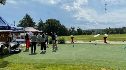 Gruppe Menschen steht auf Golfplatz, unter blauem Himmel.