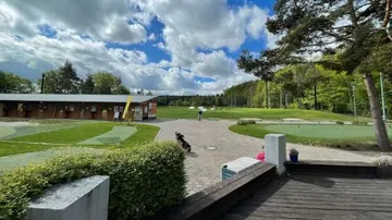 Golf course with players, surrounded by trees and clouds.