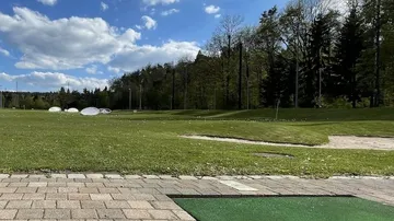 Golf course with green driving range and blue sky.