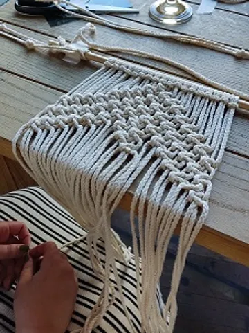 Macrame panel is knotted with hands on a table.