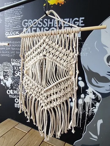 Macrame wall hanging in front of a black wall.