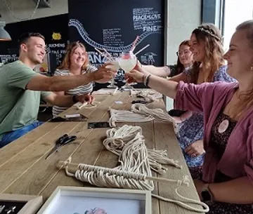 Friends toast with cocktails surrounded by rope material.