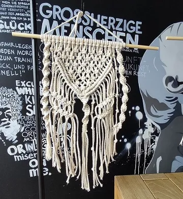 Macrame wall hanging on a pole in front of a wall.