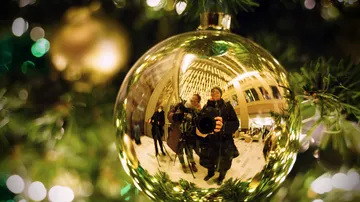Goldene Christbaumkugel reflektiert Menschen und Lichter im Hintergrund.
